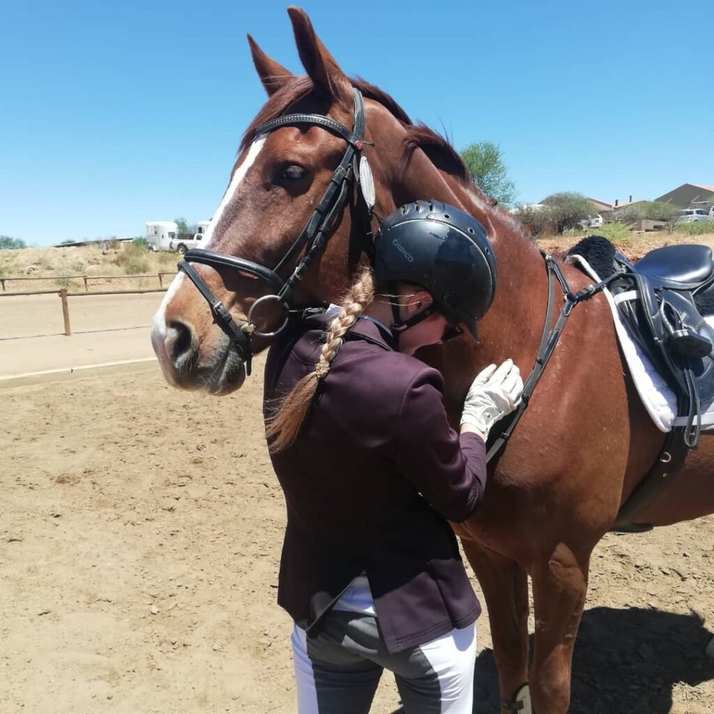 Rider in a helmet hugging a bay horse in the arena